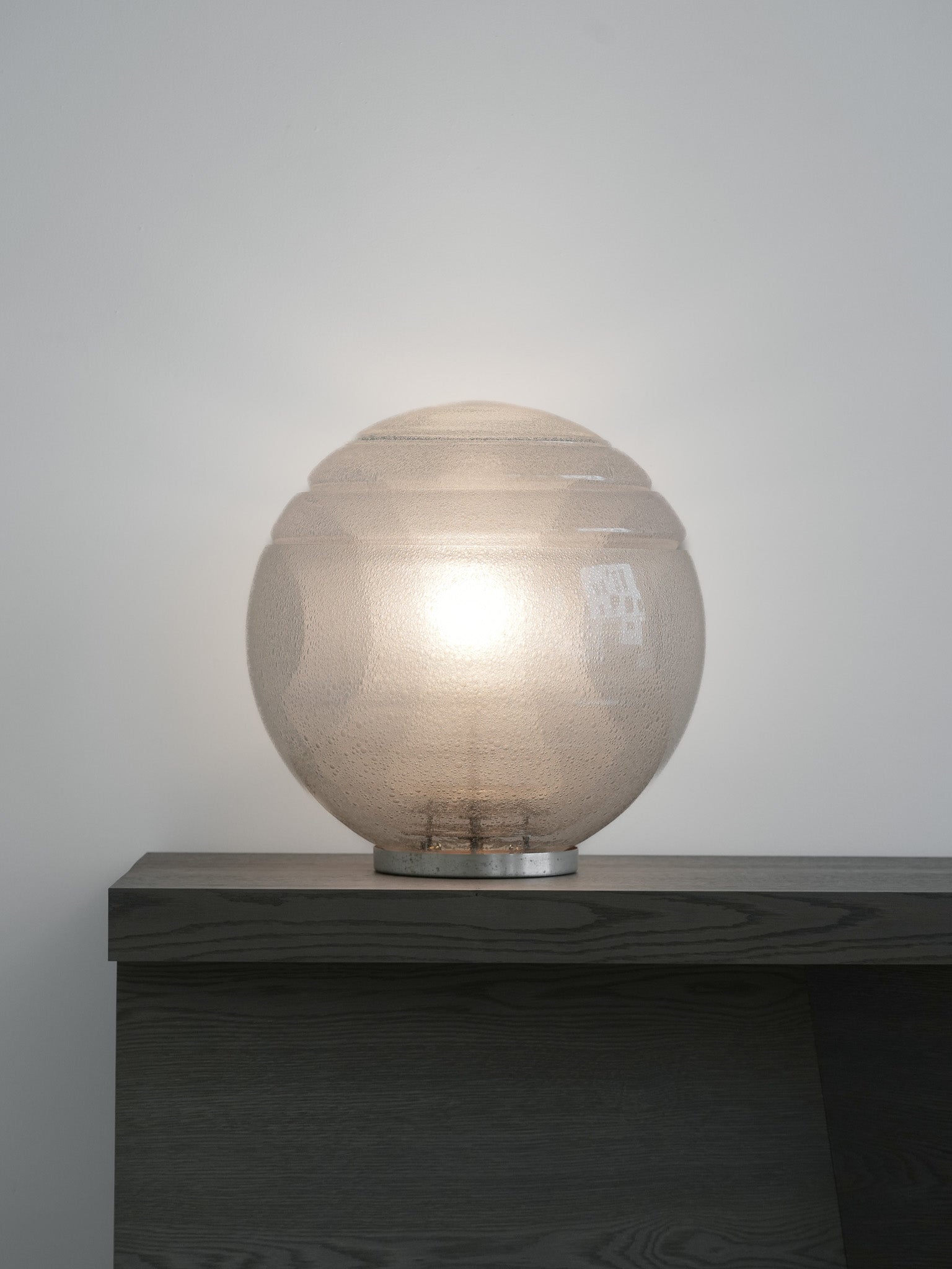 Vintage LT328 table lamp, designed by Carlo Nason for Mazzega in the 1970s. Featuring a circular metal base, this lamp is composed of four stacked glass elements that form a large, luminous globe. The air bubbles within the glass add a sense of lightness and an ethereal quality, beautifully diffusing the central light source. Available at RUE VERTE